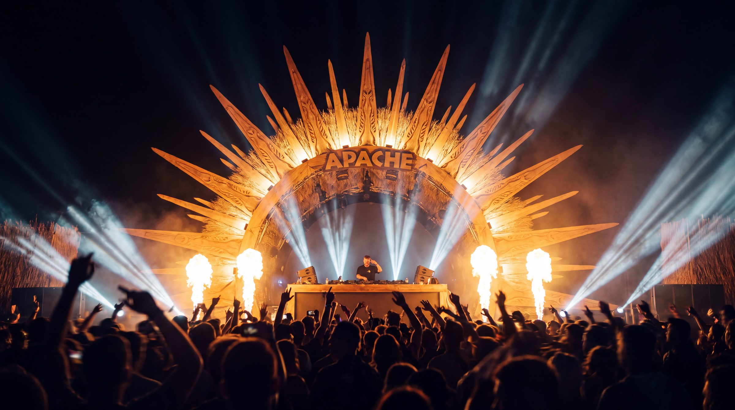 The main stage with the sculpted sun crown, beams of light and columns of fire over the crowd.